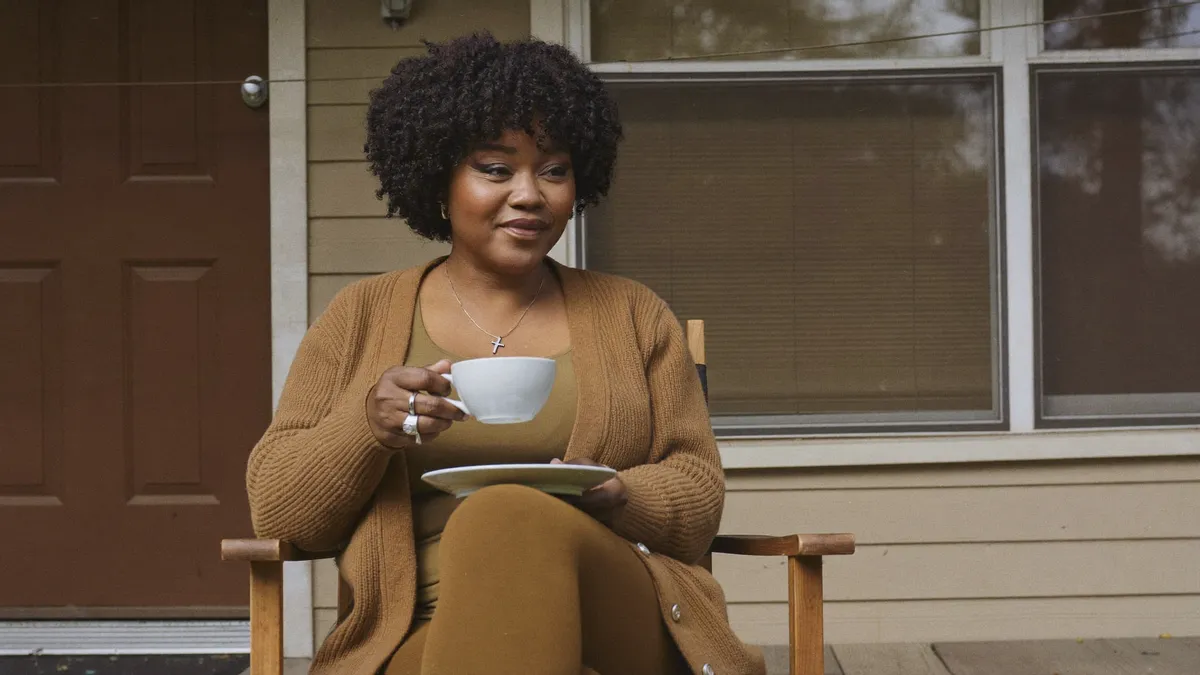 A woman relaxing on her front porch with a cup of coffee, calm and at ease