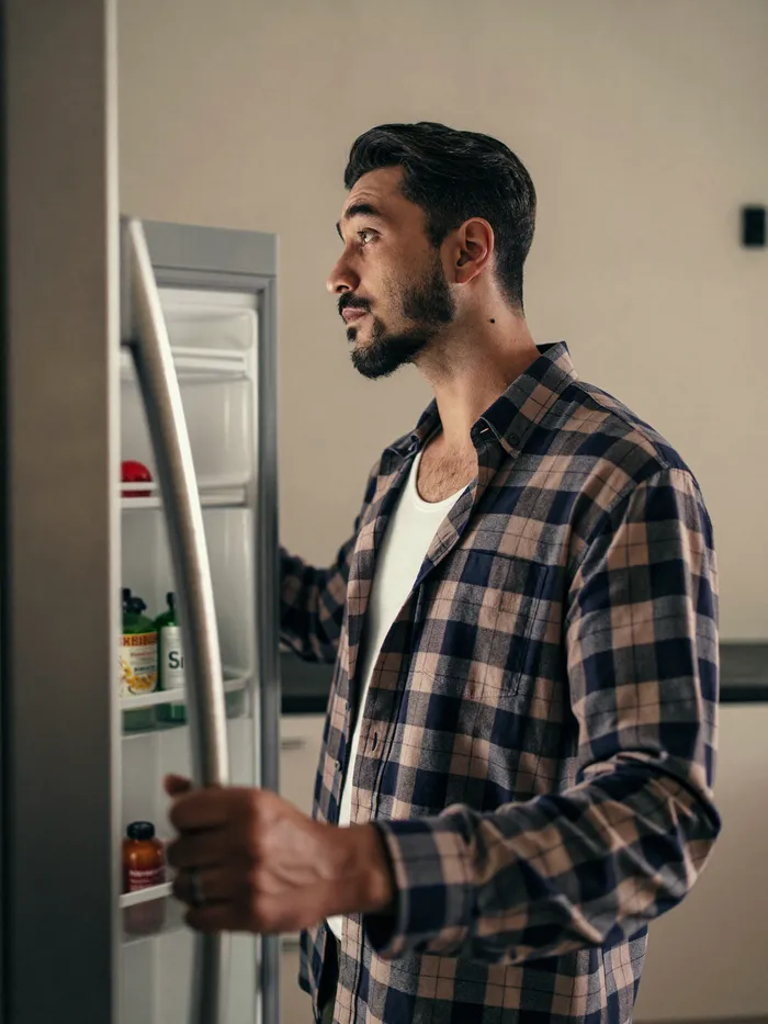 A man checking his refrigerator in the kitchen, calm despite the concern