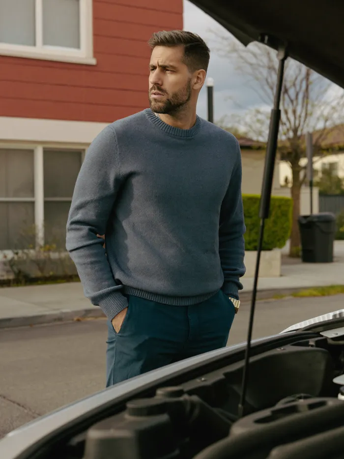 A man checking under the hood of his car on a residential street