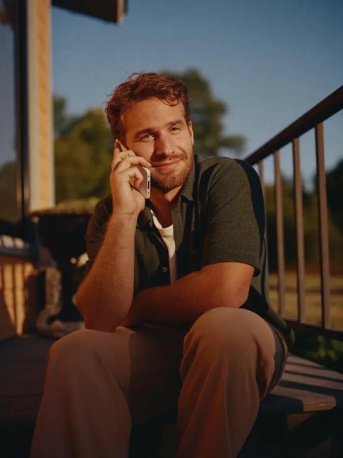 A man checking his phone on his porch in late afternoon light, relaxed and hopeful